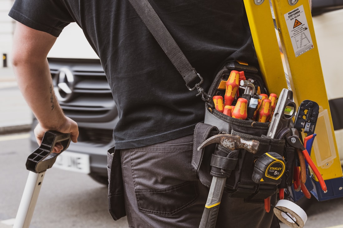 Artisan portant une ceinture à outils devant son véhicule utilitaire